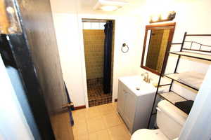 Bathroom with toilet, vanity, a tile shower, and tile patterned flooring