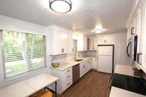 Kitchen with appliances with stainless steel finishes, a sink, light countertops, a textured ceiling, and dark wood-style floors