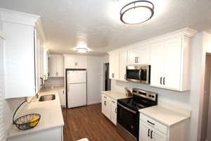 Kitchen with appliances with stainless steel finishes, white cabinets, dark wood-style flooring, light countertops, and a textured ceiling