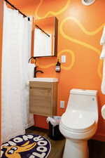 Bathroom featuring wood finished floors, toilet, vanity, and curtained shower