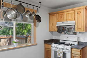 Kitchen with gas range gas stove, under cabinet range hood, and dark countertops
