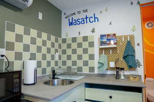 Kitchen with black microwave, a sink, a wall mounted air conditioner, decorative backsplash, and light countertops