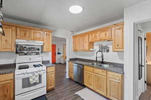 Kitchen featuring white gas range oven, a sink, dishwasher, under cabinet range hood, and dark countertops