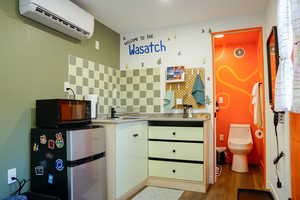 Kitchen with freestanding refrigerator, an AC wall unit, wood finished floors, black microwave, and backsplash