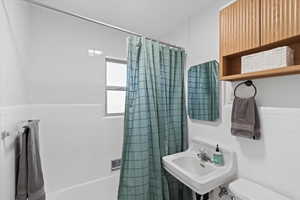 Full bath featuring shower / tub combo with curtain, a sink, toilet, and tile walls