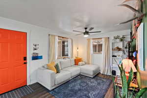 Living area with dark wood-style flooring, a ceiling fan, and baseboards
