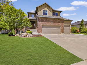 View of front of home with stucco siding, concrete driveway, a front lawn, a garage, and brick siding
