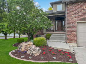 Entrance to property with brick siding, a garage, a lawn, a porch, and roof with shingles