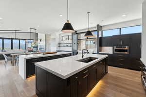 Kitchen featuring a kitchen island with sink, a sink, oven, open floor plan, and light countertops