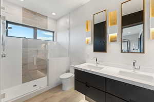 Full bath with double vanity, toilet, a stall shower, wood finished floors, and recessed lighting