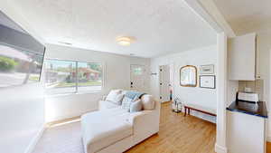 Living area with a textured ceiling, light wood finished floors, and baseboards