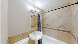 Bathroom with a textured ceiling, a chandelier, shower / bathtub combination with curtain, toilet, and a sink