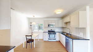 Kitchen with a sink, stainless steel appliances, light wood-style flooring, pendant lighting, and white cabinetry
