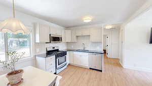 Kitchen featuring stainless steel appliances, a sink, light wood finished floors, and dark countertops