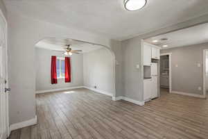 Unfurnished room with arched walkways, a textured ceiling, light wood-style floors, ceiling fan, and baseboards