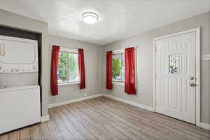 Foyer featuring stacked washer / dryer, light wood-style flooring, a textured ceiling, and baseboards