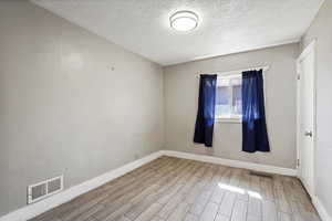 Spare room featuring wood finished floors, a textured ceiling, and baseboards