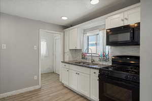 Kitchen featuring black appliances, a sink, light wood finished floors, decorative backsplash, and white cabinets