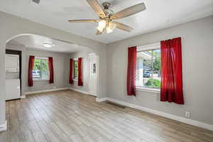 Unfurnished room with stacked washer and clothes dryer, arched walkways, wood finished floors, baseboards, and a textured ceiling