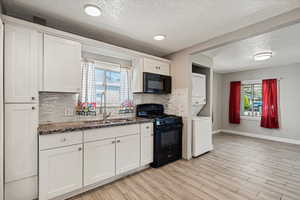Kitchen featuring black appliances, stacked washer / dryer, a sink, backsplash, and a textured ceiling