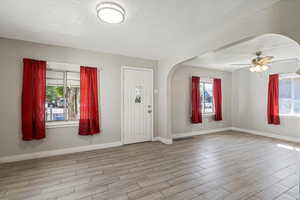 Entrance foyer featuring arched walkways, light wood-type flooring, plenty of natural light, a textured ceiling, and baseboards