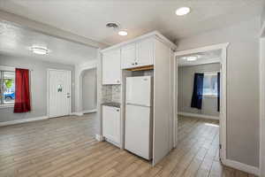 Kitchen with freestanding refrigerator, a textured ceiling, light wood-style floors, arched walkways, and white cabinets