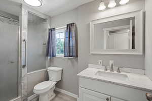 Full bath with vanity, toilet, a shower stall, baseboards, and wood finished floors