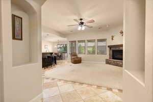 Living area with a bar, a stone fireplace, tile patterned floors, baseboards, and a ceiling fan