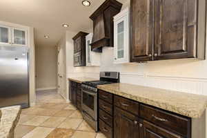 Kitchen featuring built in appliances, dark brown cabinetry, decorative backsplash, custom exhaust hood, and recessed lighting