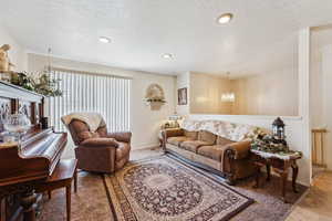 Living room featuring a chandelier, carpet flooring, a textured ceiling, baseboards, and recessed lighting