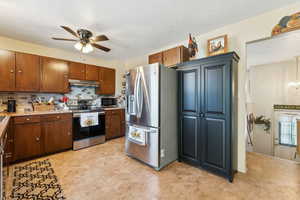 Kitchen with stainless steel appliances, under cabinet range hood, a ceiling fan, decorative backsplash, and light countertops