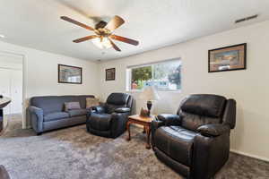 Living room with carpet floors, ceiling fan, and a textured ceiling