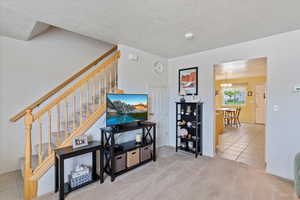Tiled living room with stairs, a textured ceiling, a chandelier, carpet floors, and baseboards