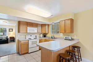 Kitchen with white appliances, a sink, a kitchen breakfast bar, a peninsula, and light countertops