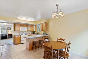 Kitchen featuring white appliances, a peninsula, a chandelier, light countertops, and light tile patterned flooring