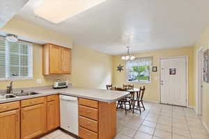 Kitchen with dishwasher, a peninsula, a sink, light tile patterned flooring, and a chandelier