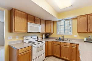 Kitchen with white appliances, a sink, light countertops, and light tile patterned floors