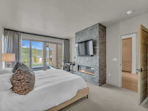 Bedroom with access to patio with hot tub, a stone fireplace, carpet flooring,