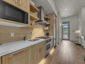 Kitchen featuring black microwave, wall chimney exhaust hood, luxury stove, open shelves, and a sink