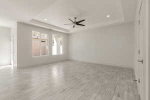 Unfurnished room featuring a tray ceiling, a ceiling fan, light wood-style floors, recessed lighting, and baseboards