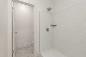 Full bathroom with a tile shower, baseboards, and wood finished floors