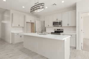 Kitchen featuring stainless steel appliances, recessed lighting, a center island with sink, baseboards, and light wood-style flooring