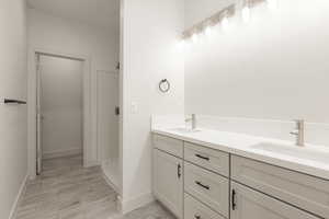 Full bathroom featuring a walk in shower, double vanity, baseboards, and wood finished floors
