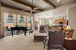 Living area with beamed ceiling, a ceiling fan, plenty of natural light, light carpet, and a chandelier