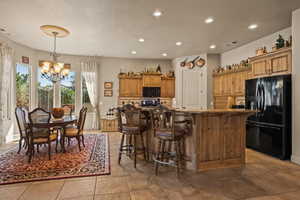 Kitchen with black appliances, a chandelier, brown cabinetry, a kitchen bar, and recessed lighting