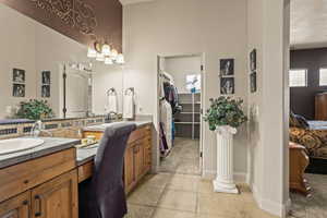 Ensuite bathroom with double vanity, tile patterned floors, a walk in closet, and baseboards