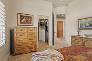 Bedroom featuring light carpet, a walk in closet, a closet, and baseboards