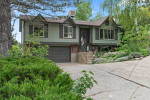 Raised ranch featuring driveway, an attached garage, brick siding, and central air condition unit