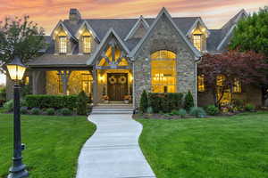 View of front of home featuring stone siding, a yard, a shingled roof, and a chimney