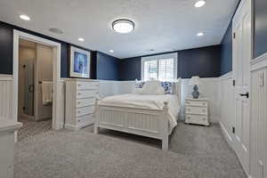 Carpeted bedroom with wainscoting, a textured ceiling, and a decorative wall